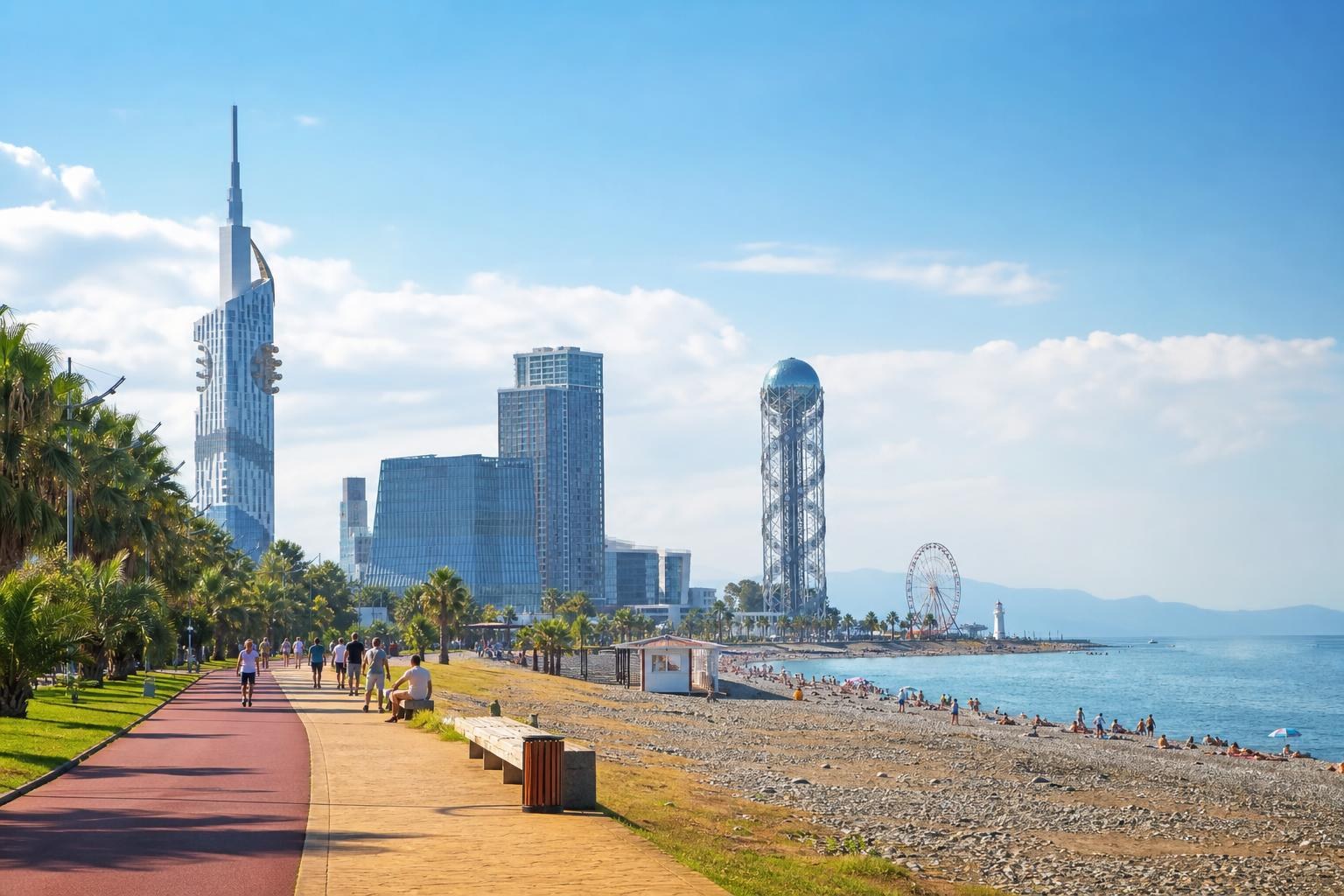 Sunny Batumi promenade featuring the Alphabetic Tower, modern skyscrapers, and a pebble beach lined with palm trees under a clear blue sky.