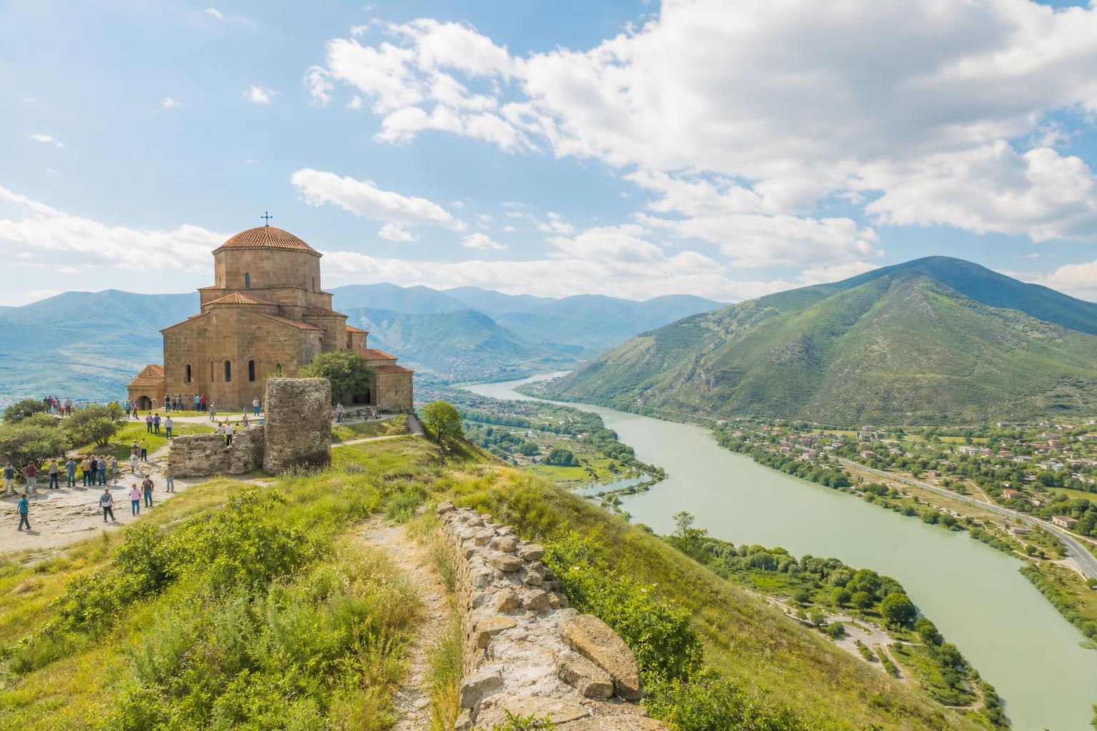 Jvari Monastery overlooking the confluence of the Mtkvari and Aragvi rivers in Mtskheta, Georgia, under a bright blue sky.