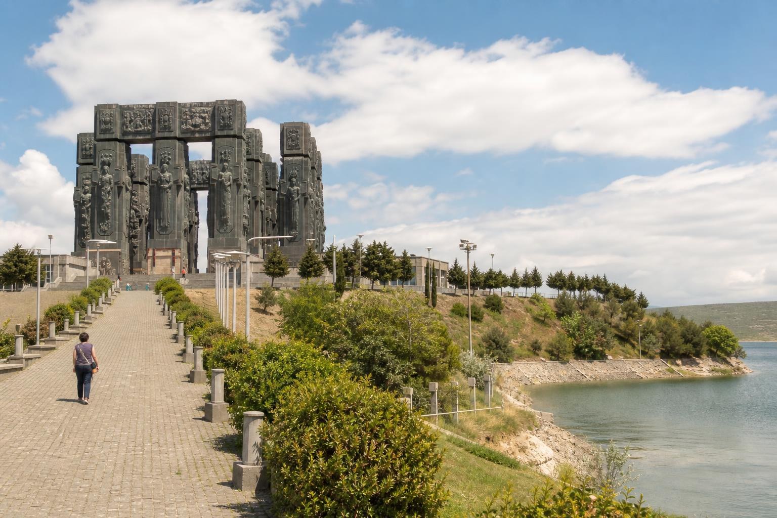 Massive bronze pillars of the Chronicle of Georgia monument overlooking the Tbilisi Sea under a bright blue sky.